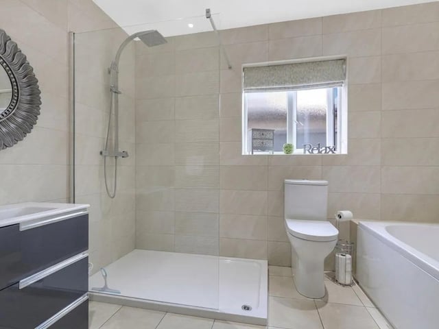 The well-appointed bathroom features a low-level flush WC, vanity-style wash basin and panelled bath with centrally positioned mixer taps, together with a walk-in shower fitted with wall-mounted rainfall and handheld shower fittings.