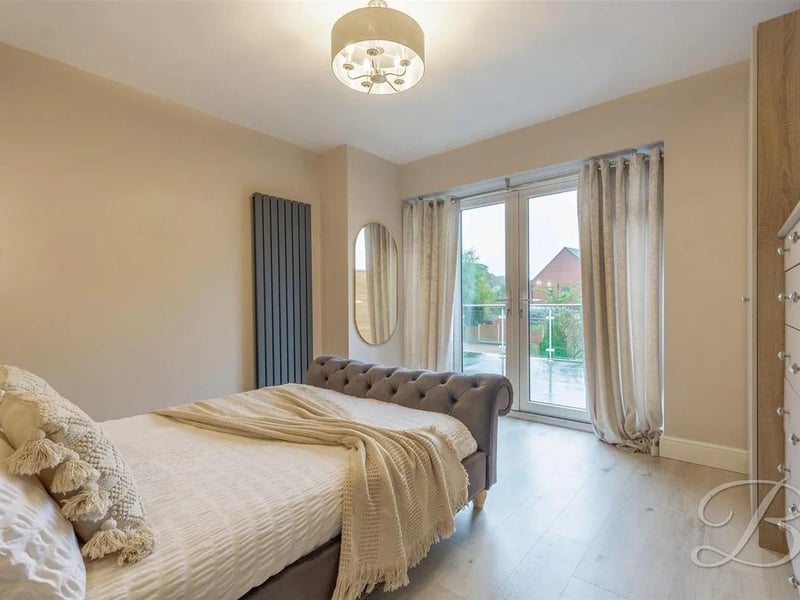 Bedroom 2 has laminate flooring, a vertical central heating radiator, and access out onto a spacious balcony with views over the rear garden.