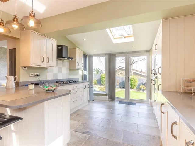 The light and bright kitchen features a range of contemporary shaker cabinets comprising wall cupboards, base units and drawers complemented by dark grey granite work surfaces.