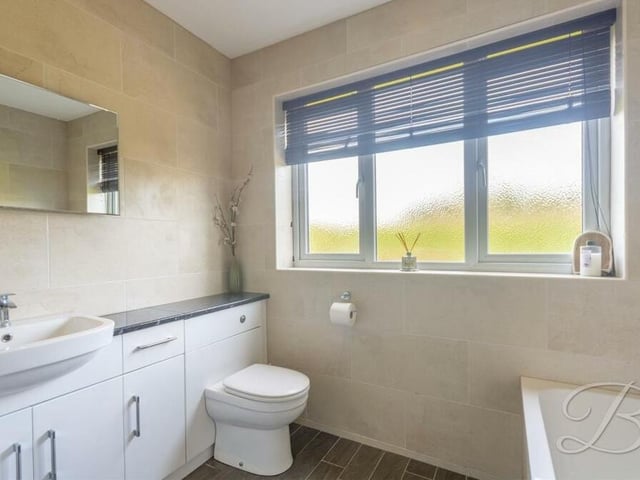Serving the bedrooms on the ground floor is this family bathroom, which includes a wash hand basin, vanity storage, full-height tiling and a low-flush WC.