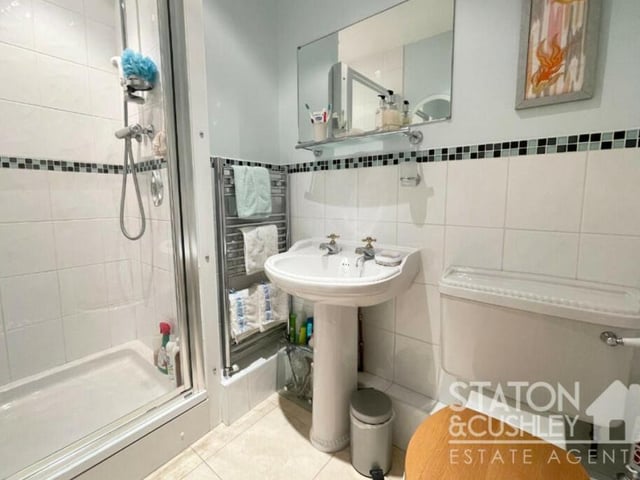 One of the downstairs bedrooms has access to this Jack and Jill shower room, which has a shower cubicle with mains shower, pedestal sink, low-flush WC, heated towel-rail and travertine marble tiled floor.
