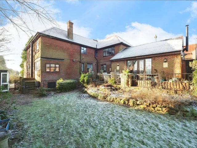 To the property's rear is a paved raised patio area with steps down to the lawned garden, borders with shrubs and trees.