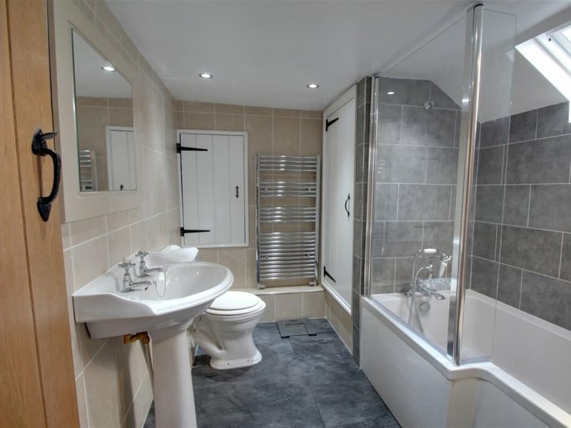 The first floor contains this stylish bathroom. A modern suite comprises a bath with shower over, a pedestal wash hand basin, low-flush WC, heated towel-rail, cupboard housing the boiler and Velux-style window.