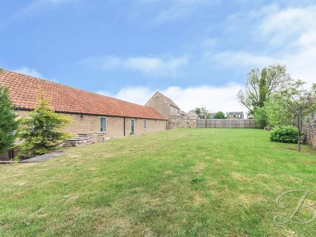 The rear garden offers a laid lawn, patio seating area, decorative shrubbery and a brick wall surround.