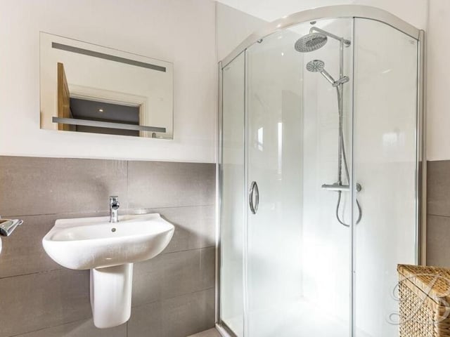 Two of the five bedrooms have the added benefit of their own en suite shower rooms. Here is the one to the master which is fitted with a modern suite in white, comprising a shower cubicle, wash basin, low-level WC, chrome, heated towel-rail, tiled floor and ceiling spotlights.