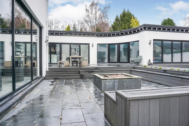 Grey decking sweeps around the property with a large square fire pit surrounded by steps and a seating area. Follow the decking to the hot tub.