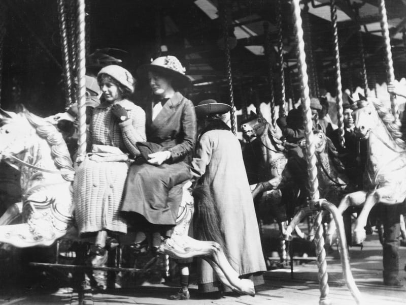 Women on a roundabout's galloping horses at the fair in 1908.