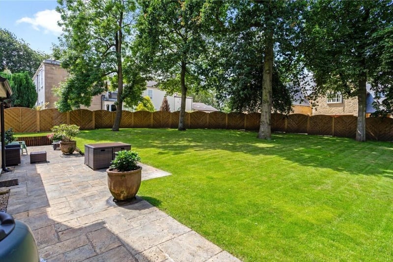 The back garden is a bonny, enclosed space, featuring not only a large patio but also a lawn surrounded by mature trees and an arched fence.