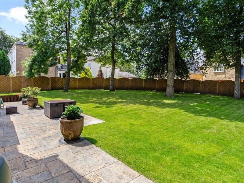 The back garden is a bonny, enclosed space, featuring not only a large patio but also a lawn surrounded by mature trees and an arched fence.