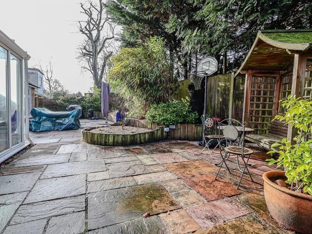 To the rear is a large, shaped Indian sandstone patio with timber-edged raised border containing a wide variety of plants and shrubs.