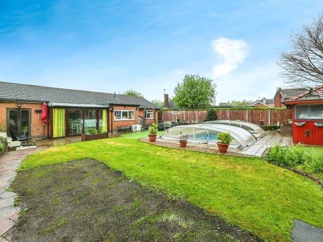 A wide shot of the rear of the Portland Road bungalow, showing the garden with its paved patio area, lawn, pool and annexe. You can also see the patio doors that open from the dining room and, to the left, another set of doors that open out from the integral garage.