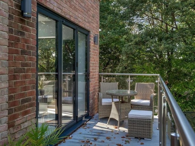 We've already seen one balcony at the £975,000 property. Here is a second, which is accessed from the living kitchen. It has a modern, glass balustrade, with a brushed stainless steel handrail, a light grey decked floor, two light points and steps leading down to the garden.