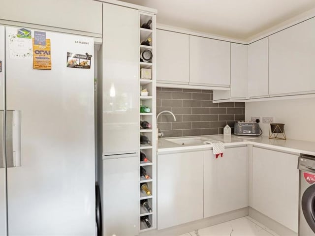 Just off the kitchen is this handy utility room, where there is plumbing for a washing machine and space for a large fridge freezer. It also features a wine rack, inset ceramic sink with mixer tap and built-in drainer, and high-gloss cabinets.