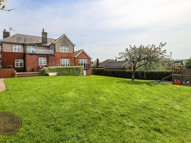 Stepping outside now, and here is a view of the property from the rear. The private, south-facing garden is dominated by an extensive lawn, with flowerbed borders, plants and shrubs. To the right, you can see a barked play area too.
