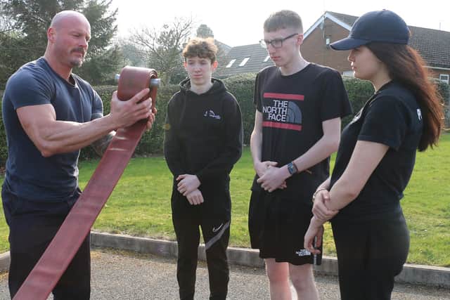 Crew manager Ian Edmonds shows students, from left, Baily Ford, Adam Tomlinson and Charlie-Francis Massey how to uncoil a hose.