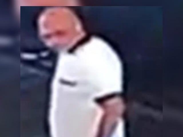 Bald man, white t-shirt with black collar and cuffs, jeans.