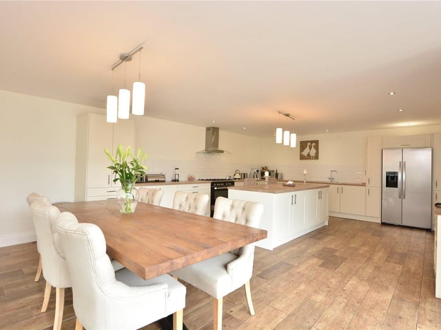 The bright and airy kitchen diner features modern fitted cupboards with integrated appliances, a central island, a separate dining area, and a feature barn window.