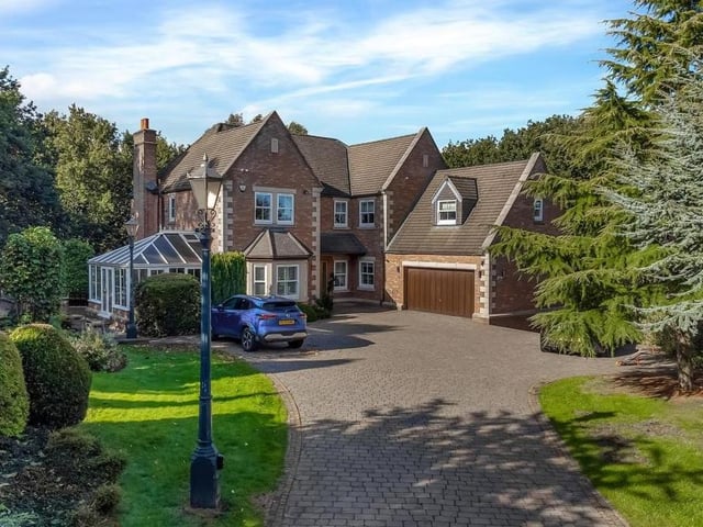 The inviting facade of the house, with its long driveway, lined by trees and shrubs, and large garage.