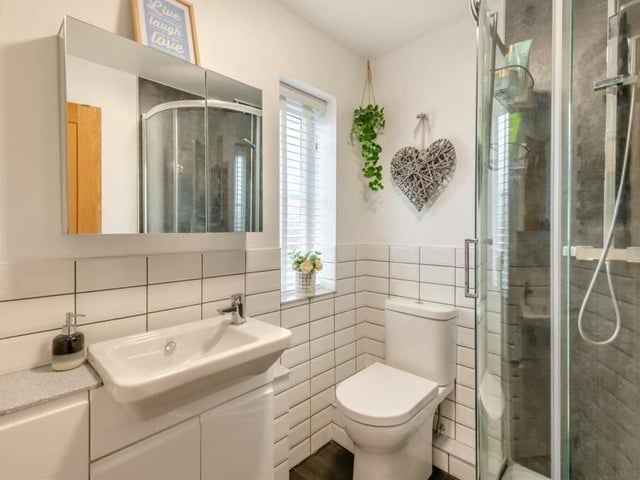 The en suite to the master is a striking three-piece white suite with chrome fittings, consisting of a shower enclosure with aquaboard splashback, a vanity unit with inset Vitra wash hand basin, mixer tap, work surfaces and storage cupboards beneath, and also a low-flush WC. The walls are partly tiled and there's a graphite, heated towel-rail.