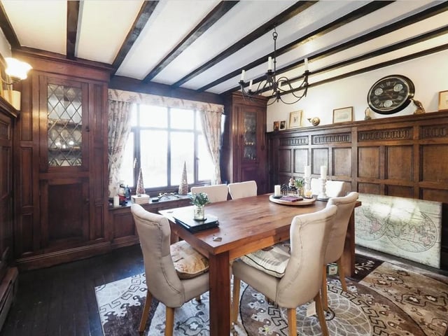 The dining room has panelled walls, a beamed ceiling, a brick fireplace with an open fire for logs and coals, and an exposed wood floor.