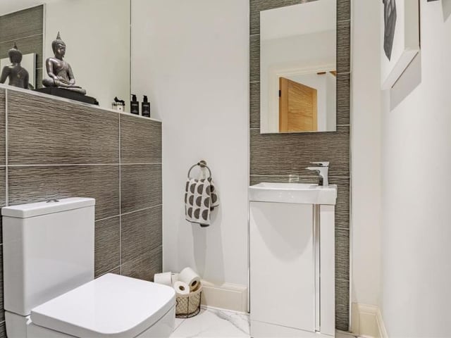 The ground floor also includes this downstairs toilet, which has a modern two-piece suite comprising a low-flush WC and vanity unit with inset wash hand basin and storage cupboard beneath. Even this room has heating underneath its porcelain tiled floor.