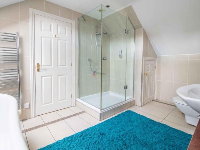 The en suite to the main bedroom also includes this modern glass shower cubicle with an Aqualisa shower. The wash hand basin and WC are built into a vanity unit, while there is a storage cupboard at the end of the room.