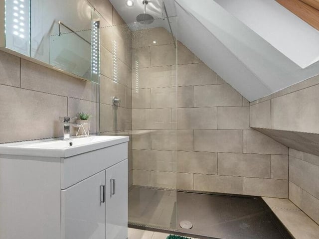 Here is the en suite shower room to the master bedroom. Modern and beautifully presented, with contemporary tiling, it boasts a double walk-in shower enclosure with floor-to-ceiling glass and an internally plumbed chrome shower. There is also a wall-hung wash hand basin with chrome mixer tap and inset storage, a low-flush WC and ceiling spotlights.