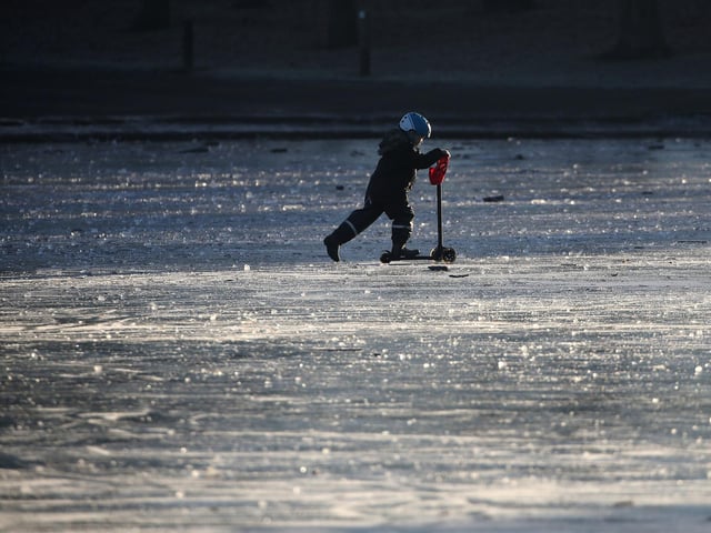 A child pushes a scooter on a frozen pond at Victoria Park