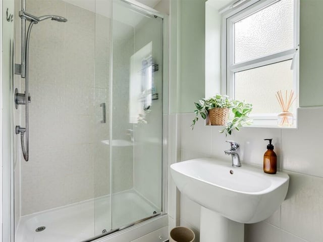 The en suite to the master bedroom includes a shower enclosure with wall-mounted shower fixture and sliding door. There is also a pedestal wash basin.