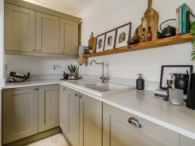 The kitchen features a range of contemporary shaker cabinets in contrasting colours, comprising wall cupboards, base units and drawers, with marble-effect work surfaces. Inset is a one-and-a-half-bowl ceramic sink with drainer and mixer tap.
