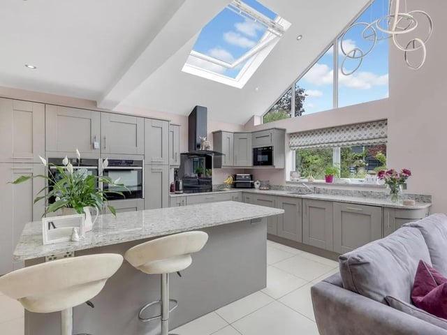 The kitchen features a range of fitted wall and base units with worktops, along with a central island and breakfast bar. Integrated appliances include a sink, two ovens, hob with extractor, dishwasher and microwave, with space for a fridge freezer.
