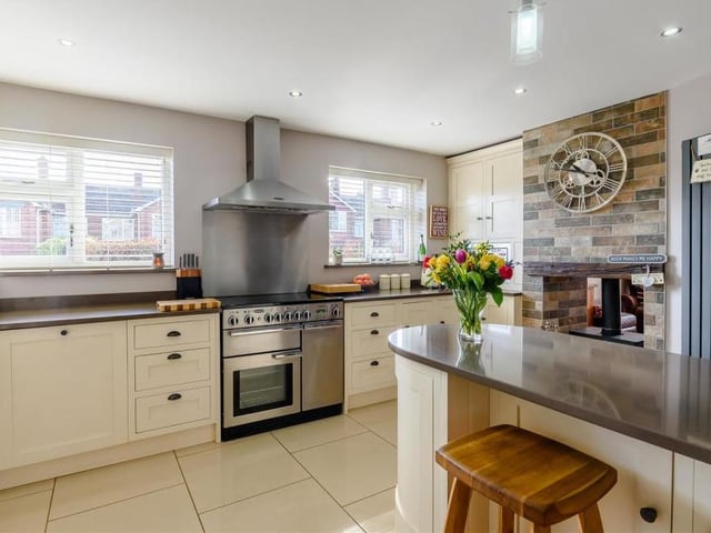 Another view of the slick and sleek kitchen/breakfast room, which boasts an integrated microwave and dishwasher and has space for a range cooker and American fridge freezer. The room also features a dual log-burner with granite hearth, a tiled floor, ceiling spotlights, additional lights above the island and two double-glazed windows to the side of the house.