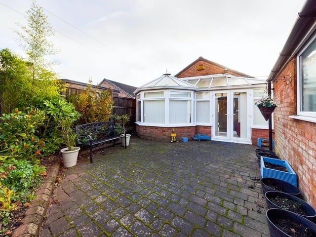 This view of the conservatory from the outside shows the low-maintenance garden at the back of the bungalow. It features block paving, mature shrubs and a detached garage with lighting and electricity.