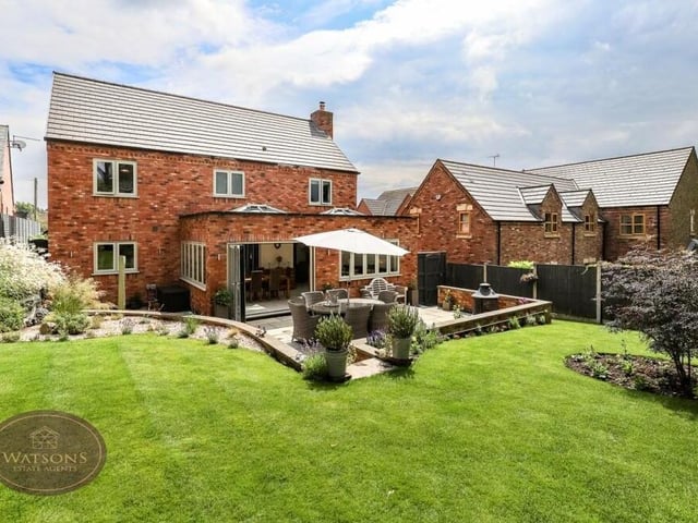 As we step outside, let's delight at a view of the back of the property, as seen from the landscaped rear garden. You can see how doors from the orangery open on to a patio area.