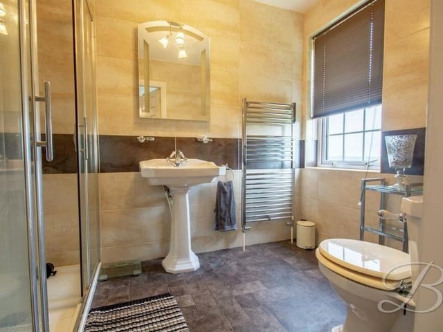 The main bedroom has access to this sparkling en suite, which comprises an enclosed shower, pedestal sink, low-flush WC, chrome heated towel-rail and full-height tiling.