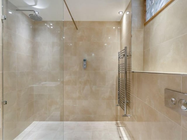 Here is the en suite wet room to the master bedroom. A modern, well appointed space by Porcelanosa, it is dominated by a walk-in, tiled shower with a remote-controlled, wall-mounted Grohe rainfall shower. There is also a wall-hung wash hand basin, tiled shelf above, mirror, wall-hung low-flush WC, chrome heated towel-rail and ceiling spotlights.