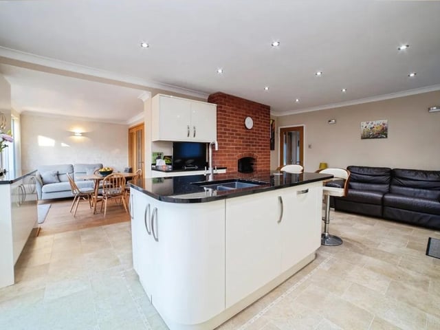 The modern and sleek kitchen features an integrated double oven, extractor hood, generous work surfaces, and a central island with sink and mixer taps.