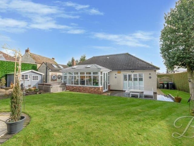 Let's step outside now and begin with a view of the back of the bungalow. It shows the conservatory and also part of the rear garden, with its lawn and storage shed.