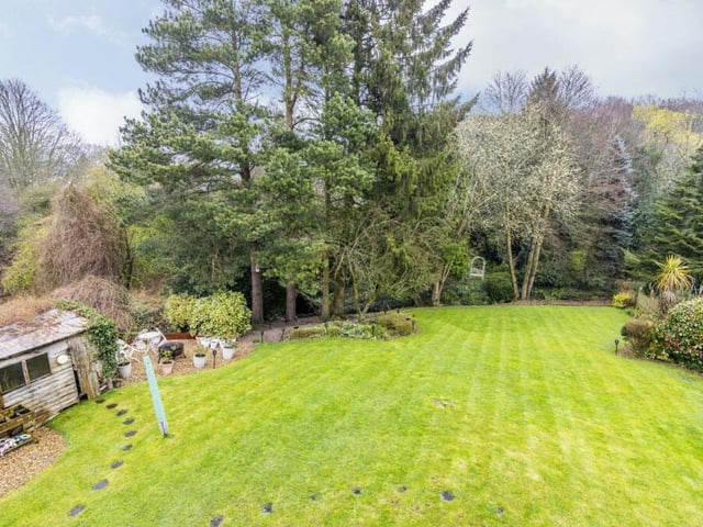 A sprawling lawn, surrounded by trees and mature shrubs, is a key feature of the large back garden