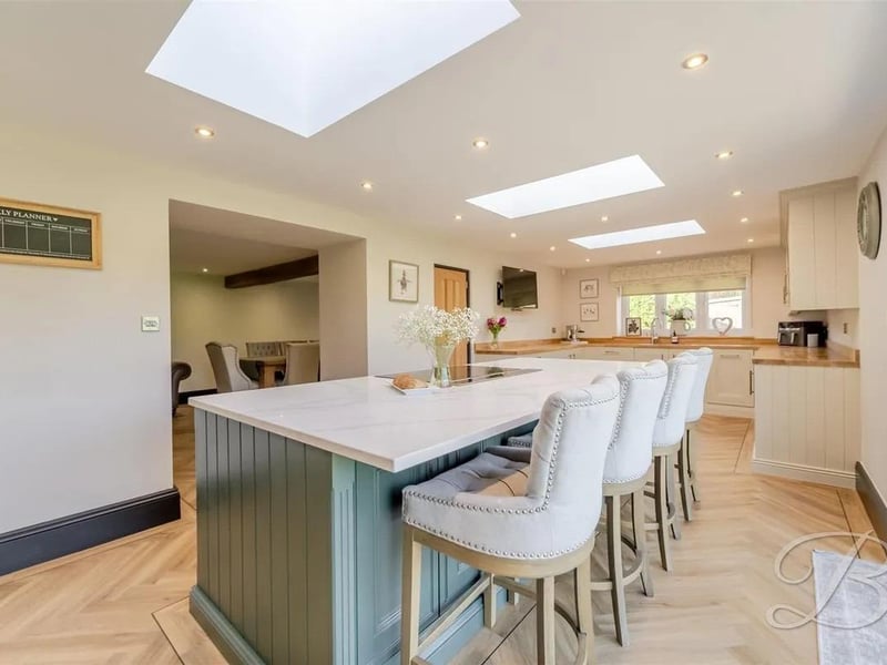 At the heart of the room sits a central island with a breakfast bar, ideal for casual dining and socialising. Natural light flows in through a side window, while bifold doors open onto the rear garden, creating a seamless connection between indoor and outdoor living.