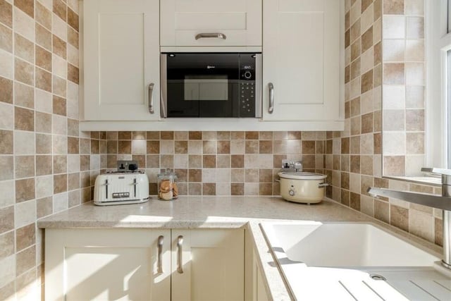 The kitchen is fitted with a range of modern, cream shaker cabinets, comprising wall cupboards, base units and drawers with brushed metal handles, all complemented by quartz-effect work surfaces. There's also an inset sink with drainer and mixer tap.