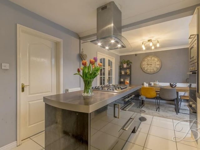 The superb kitchen features an island with five-ring hob, and a fabulous wine fridge. In the background, you can see the dining area, which accommodates a large table and chairs for family meals.