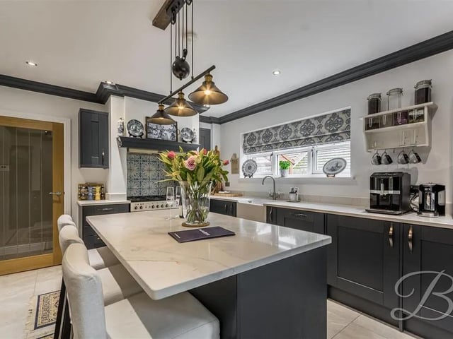 The kitchen features a range of attractive shaker style wall and base units with complementary quartz worktop over, Belfast sink with mixer tap, alcove recessed freestanding range cooker with five burner hob and extractor fan above, integrated dishwasher, two integrated fridges, breakfast bar with additional storage, matching coving, downlights, underfloor heating, central heating radiator and two windows to the rear and side elevation.