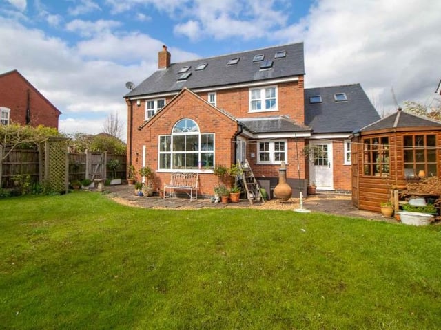This is how the property looks from the rear, showing an enclosed garden, mainly laid to lawn but also with a patio area and a cute, wooden summer house.