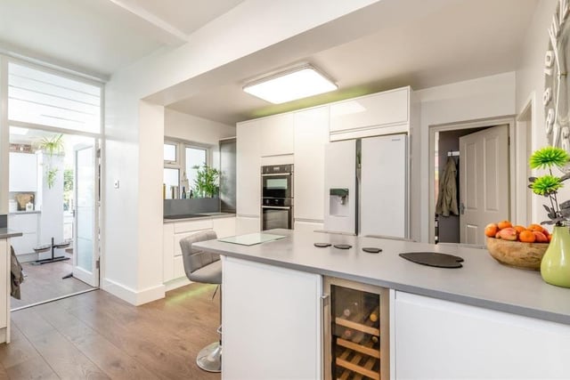 The kitchen/breakfast room features a range of modern, high-gloss white cabinets, with wall cupboards, base units, drawers and quartz worktops. A good-sized island or breakfast bar has matching cabinets and worktops, plus space for stools underneath.