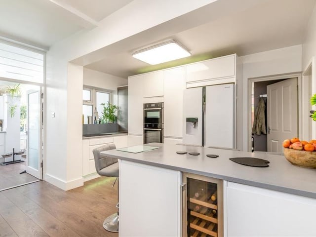 The kitchen/breakfast room features a range of modern, high-gloss white cabinets, with wall cupboards, base units, drawers and quartz worktops. A good-sized island or breakfast bar has matching cabinets and worktops, plus space for stools underneath.