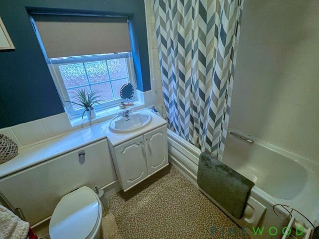 The family bathroom on the first floor is equipped with a bath tub with electric shower over and shower curtain, a vanity-style sink, close-coupled WC and vinyl flooring.