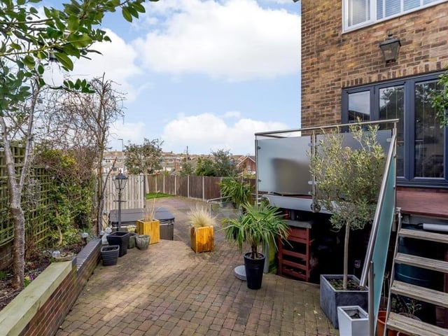 Let's take a look outside now, and this is the back garden, which includes raised flowerbeds and extensive block paving. An enclosed area has steps leading up to the balcony off the dining room, with a useful log store underneath.
