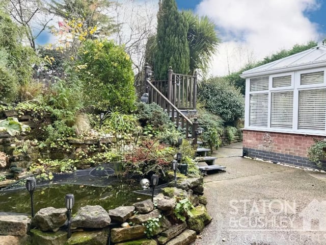 Highlights in the garden include numerous seating areas, a designated hot tub space, a vegetable garden, greenhouse, and a charming two-tier pond.