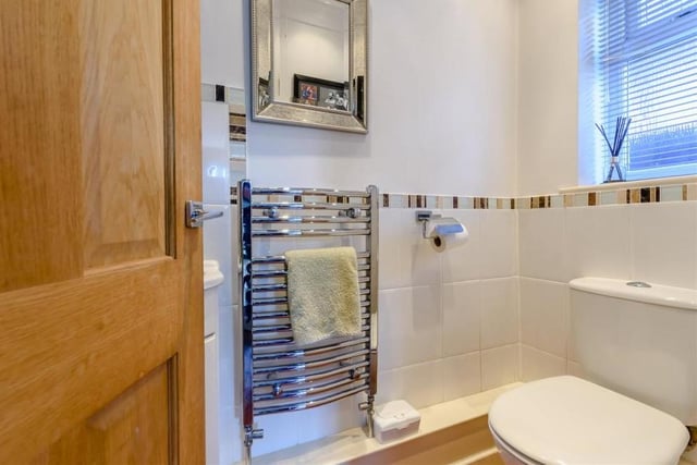Off the rear lobby, at the far end of the hallway, is this downstairs loo. It comprises a low-flush WC, corner wash hand basin with mixer tap and storage cupboard beneath, chrome, heated towel-rail, part-tiled walls and ceiling spotlights.